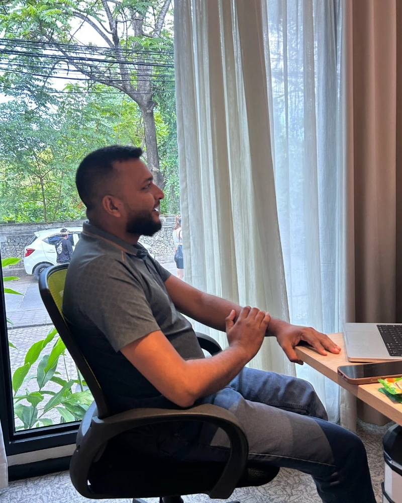 Shameem at a desk by a tall window, mid-conversation
