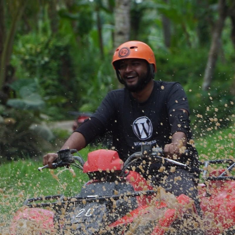Shameem riding an ATV through mud in a WordPress T-shirt and an orange helmet