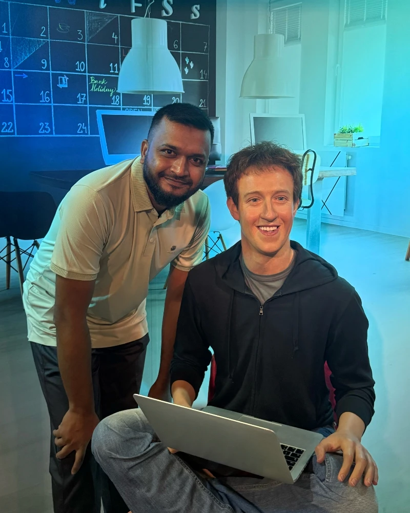 Shameem posing next to someone working on a laptop in a blue-lit room