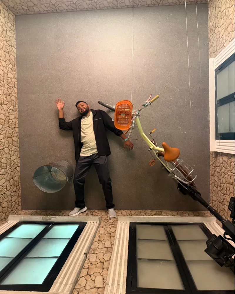 Shameem waving beside a bicycle sculpture mounted on a wall