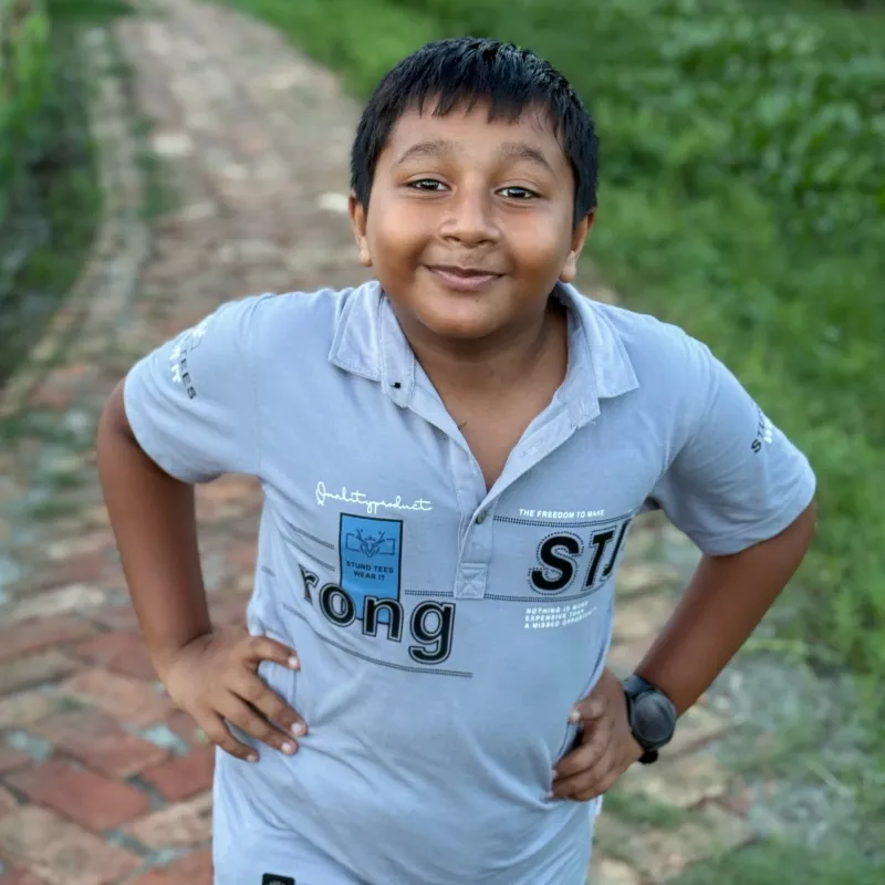A smiling boy standing on a garden path, hands on his hips