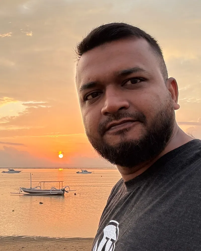 A selfie at sunset on a beach, with a boat on the water behind