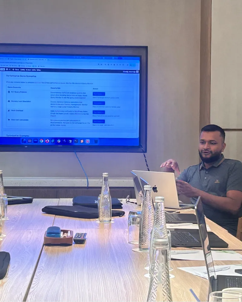 Shameem at a meeting table with laptops and a screen behind